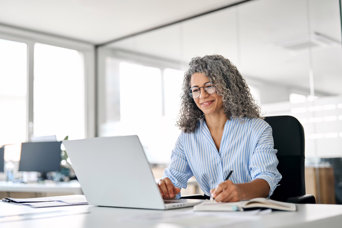 Image shows a woman seated and working on her laptop