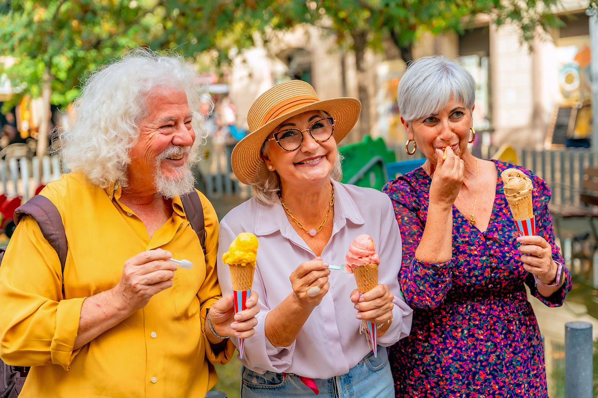 Image shows three senior travellers, each enjoying an ice cream on a sunny city street